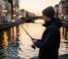 Un jeune pêcheur urbain pratiquant le street fishing sur les quais d'un canal en ville au coucher du soleil